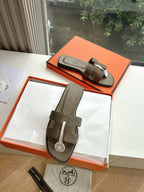 Pair of dark taupe leather slide sandals with wide front strap and logo medallion