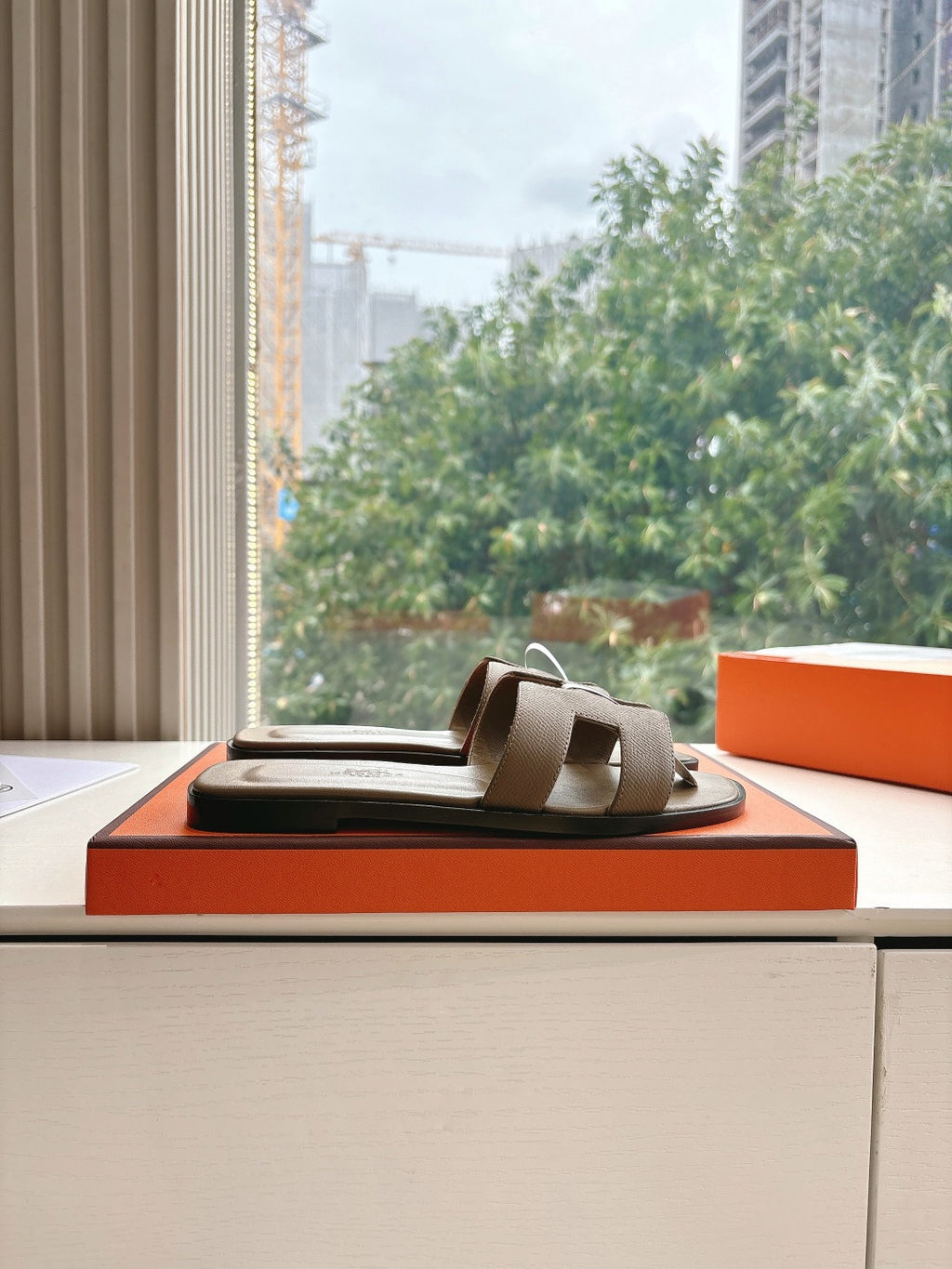 Dark taupe leather slide sandals with single front strap on orange shoebox