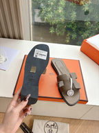 Dark taupe leather slide sandals with textured sole and logo label on box