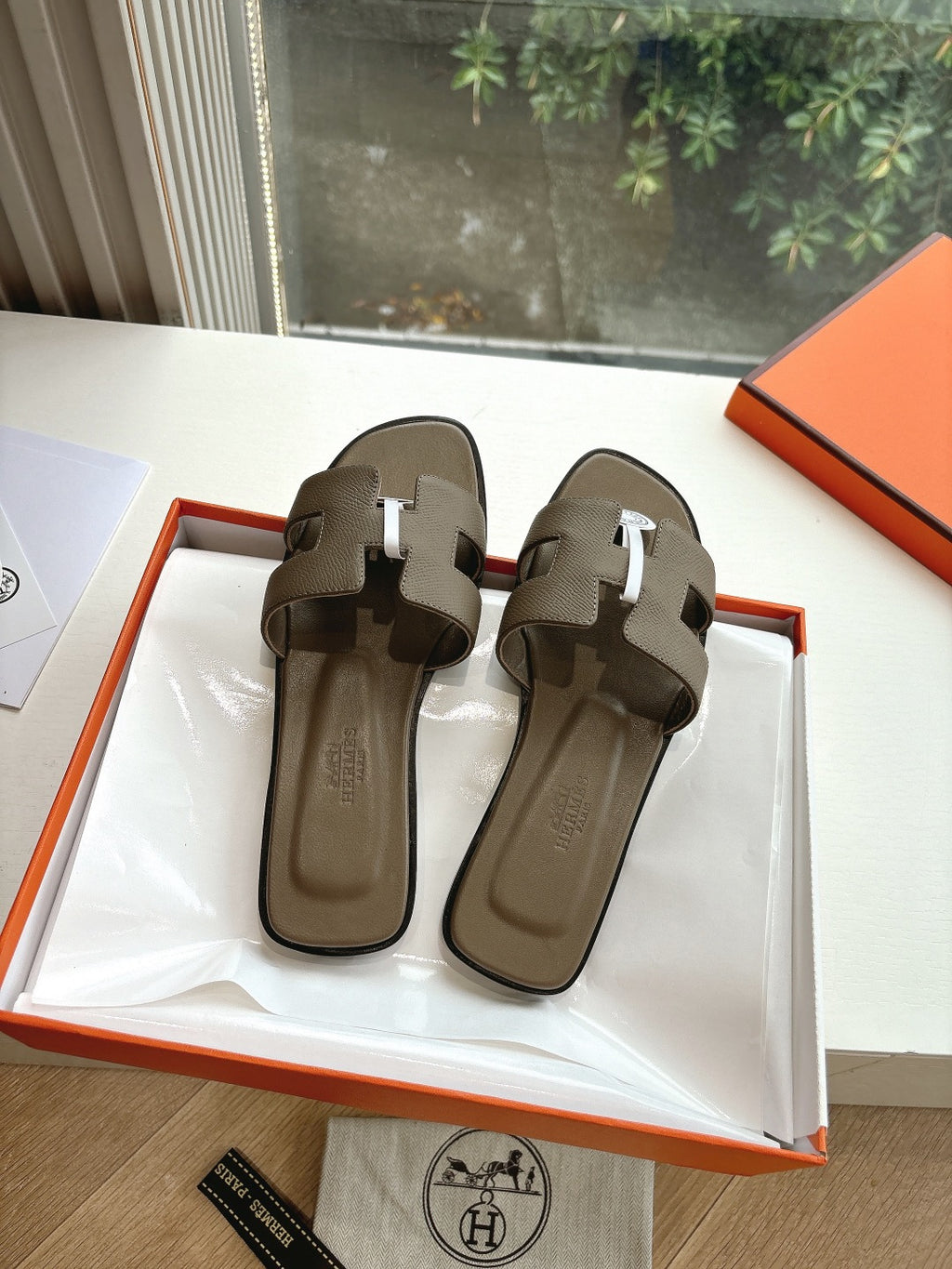 Dark taupe leather slide sandals with two front straps and round logo emblem