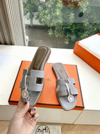 Hermes slide sandals on box, light gray textured leather with H emblem buckle