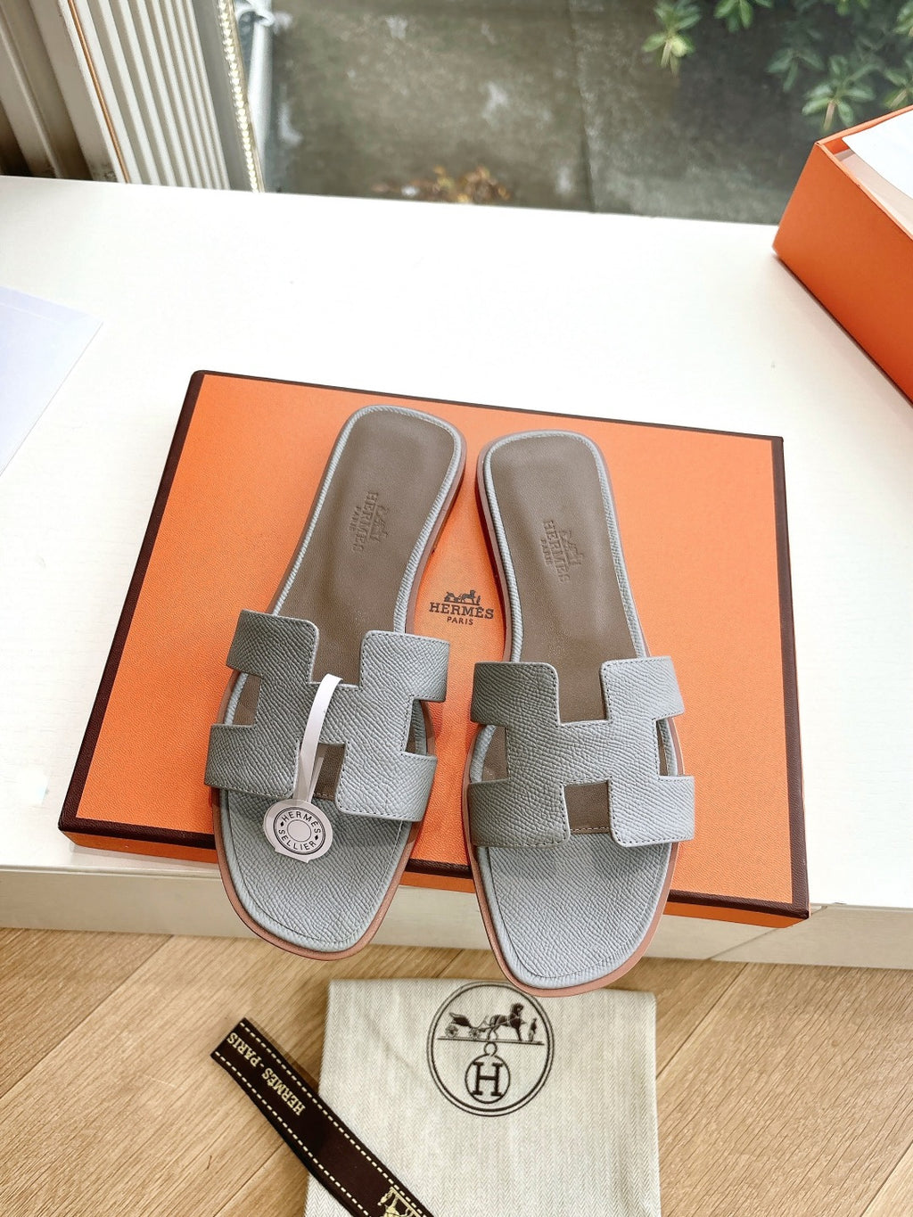 Hermes grey slide sandals pair with two wide crossover straps on orange box