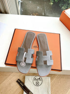 Hermes grey slide sandals pair with two wide crossover straps on orange box