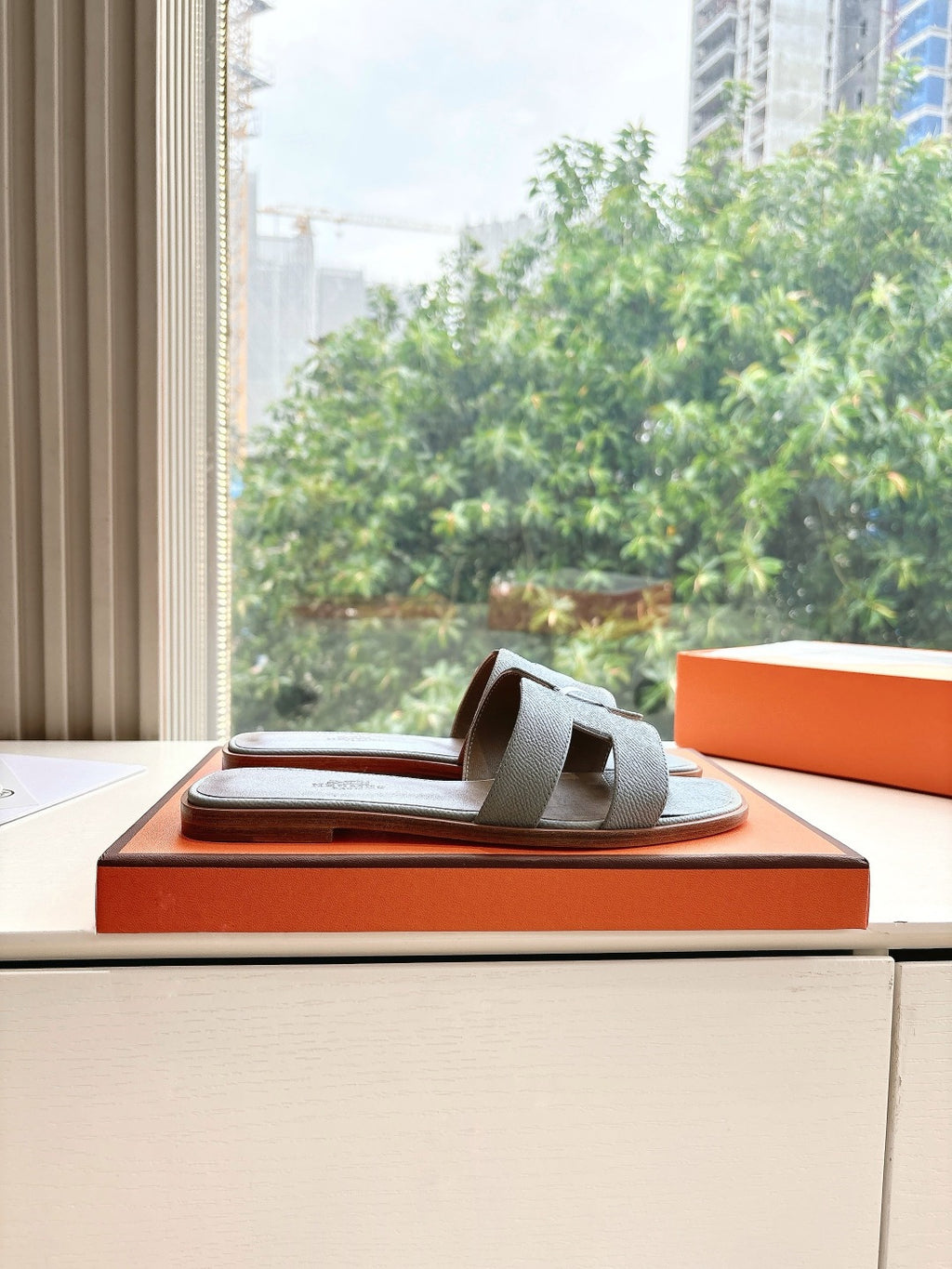 Hermes grey slide sandals displayed on orange shoebox, open-toe single pair