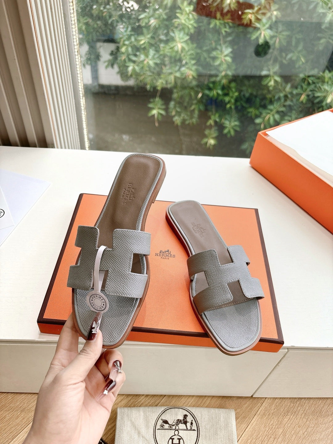Hermes grey slide sandals held in hand, two wide straps with circular logo