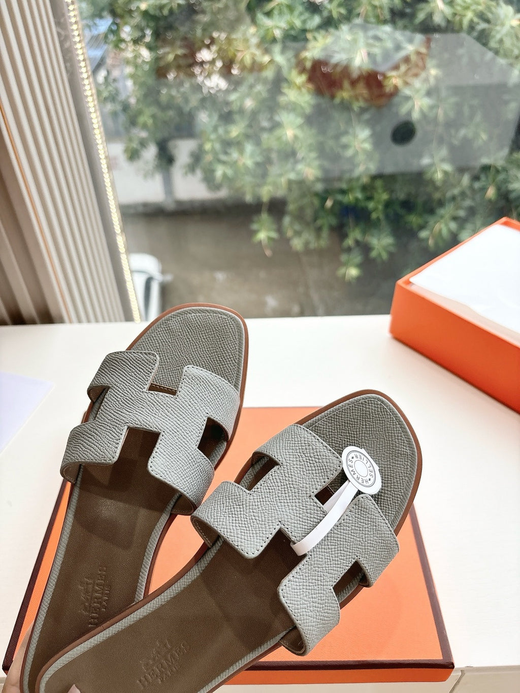Hermes grey slide sandals close-up, textured straps with circular logo badge