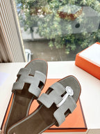 Hermes grey slide sandals close-up, textured straps with circular logo badge