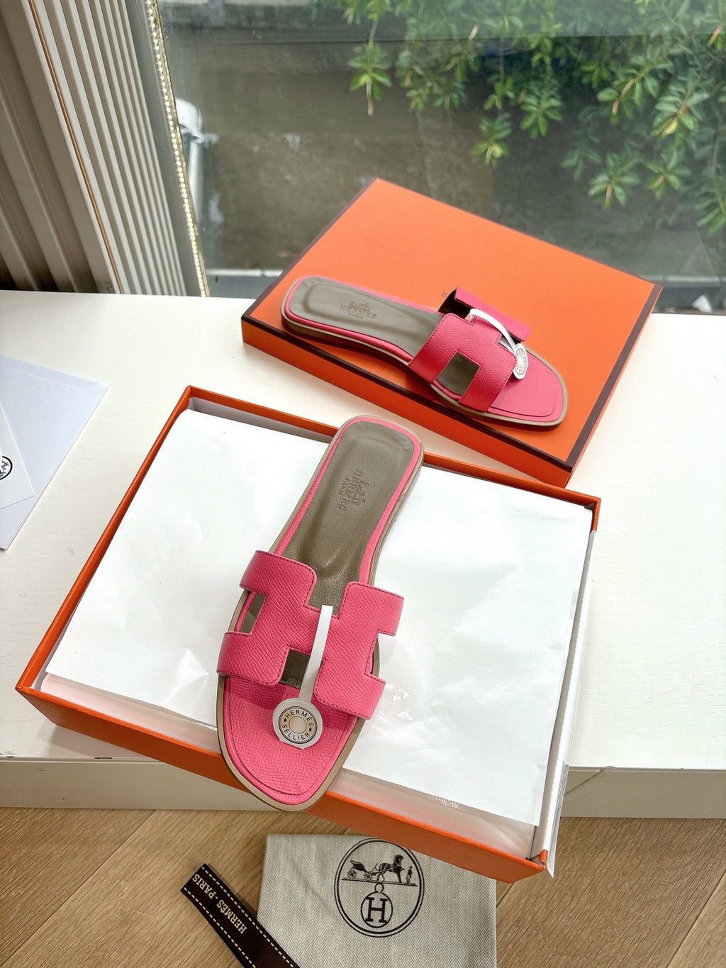 Pink leather slide sandals with two-bar strap and circular logo emblem, in box