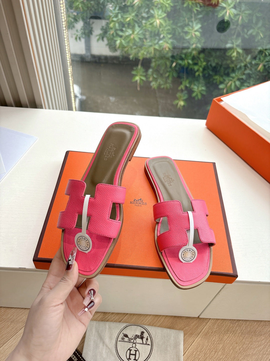 Hermes pink slide sandals with two straps and circular emblem buckle, held in box