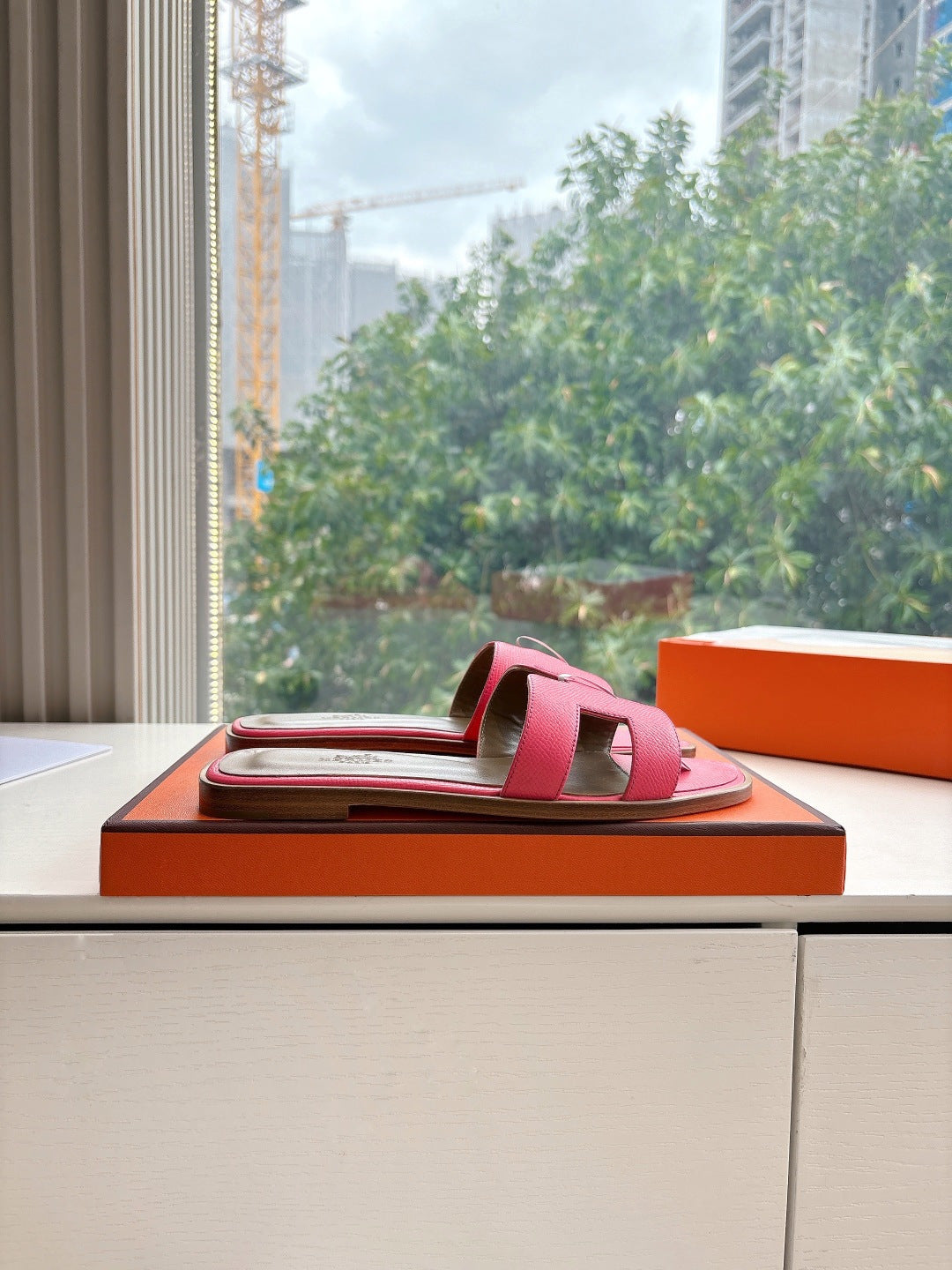 Pink leather slide sandal with open toe and adjustable strap, on display box