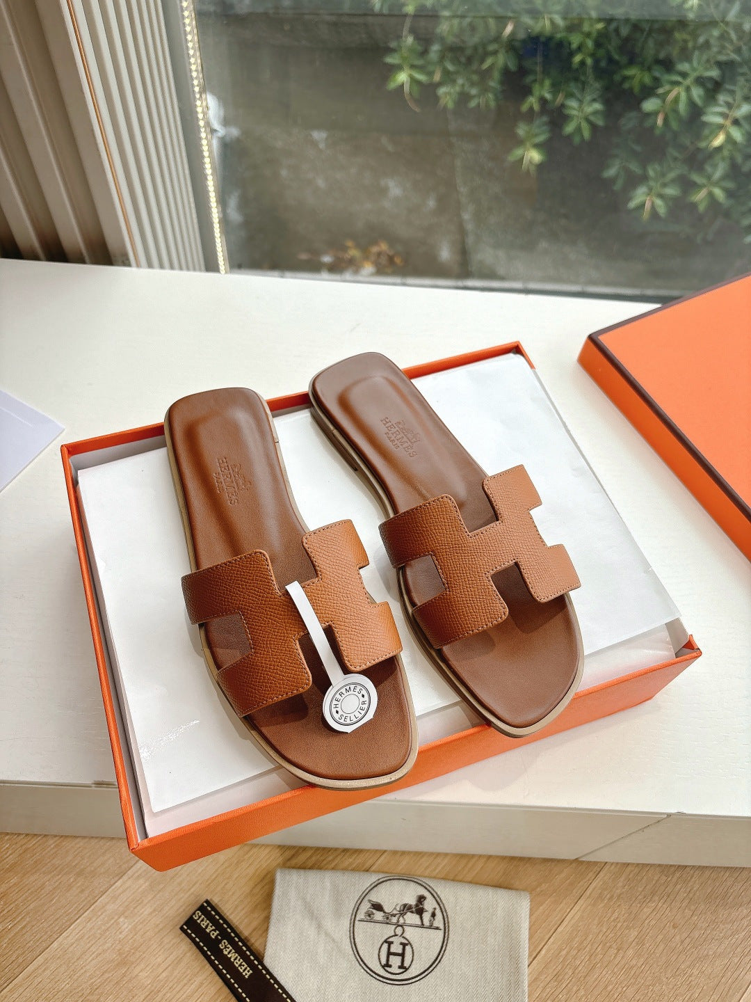 Hermes tan slip-on sandals with geometric strap design and round logo medallion