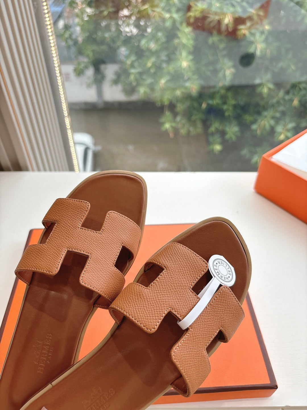 Hermes tan slip-on sandals with H-style strap design and round white logo medallion