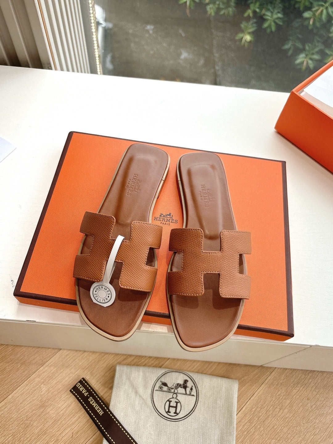 Hermes tan slip-on sandals with geometric strap design and round logo medallion