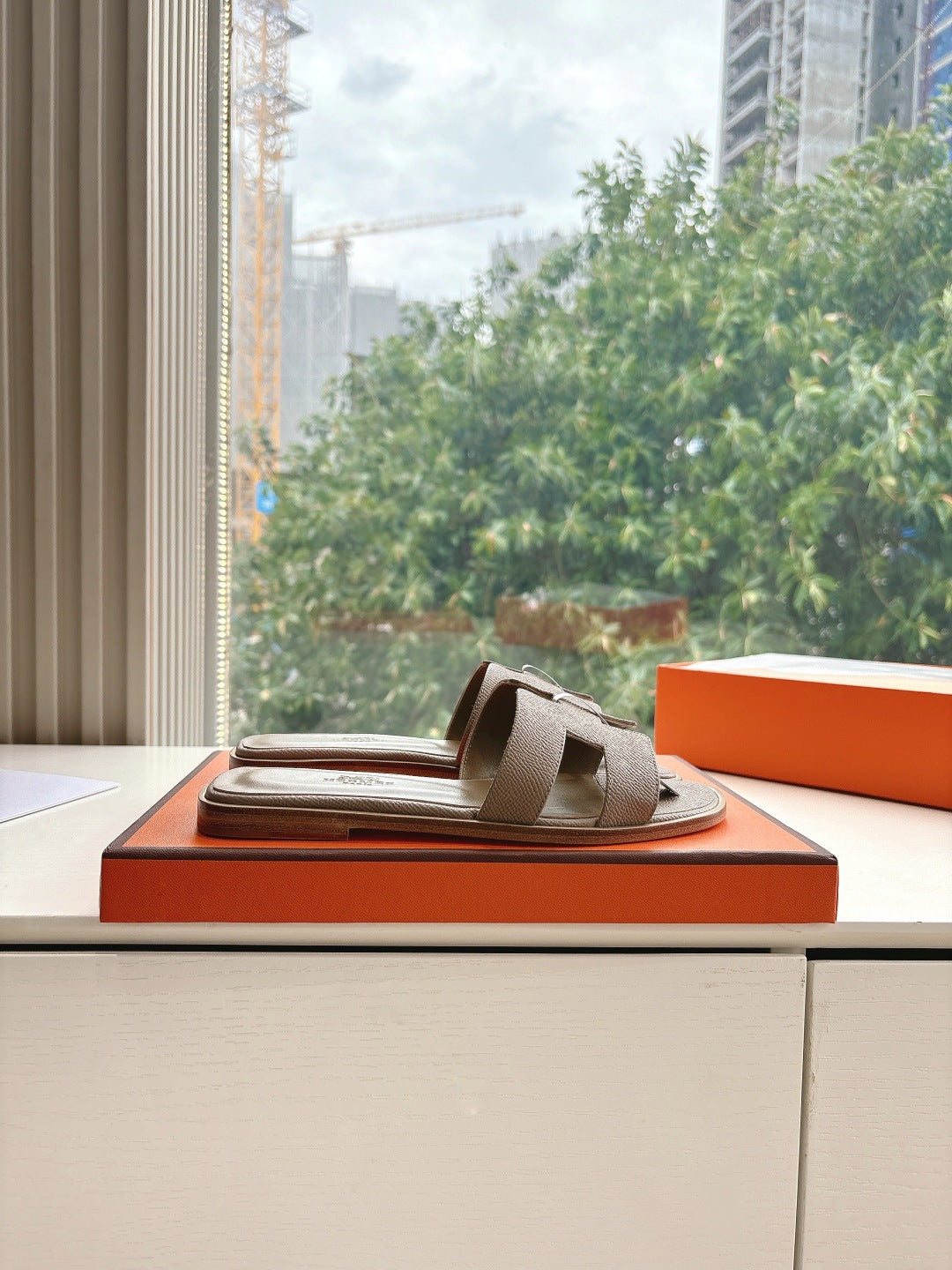 Taupe Hermès slide sandals on orange shoebox, single sandal with round logo medallion