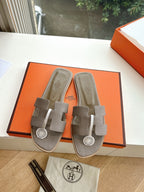 Taupe Hermès slide sandals on box, with adjustable strap and round logo medallion