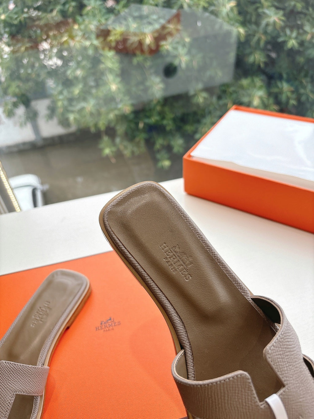 Taupe Hermès slide sandal close-up, open toe with adjustable strap and logo medallion