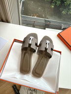 Taupe Hermès slide sandals pair view with white strap details and round logo medallion