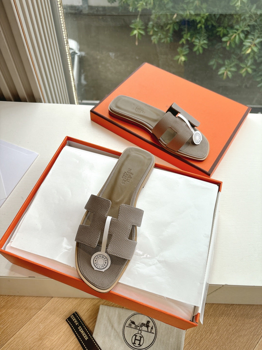 Taupe Hermès slide sandals with white strap accent and round logo medallion