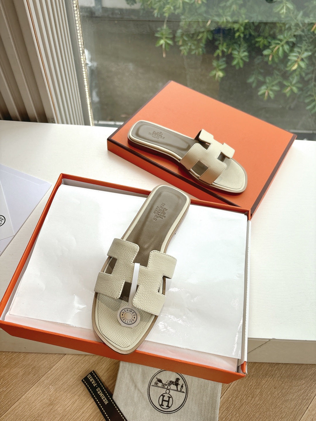 Hermes slide sandals in light beige with buckle-style strap detail and logo charm