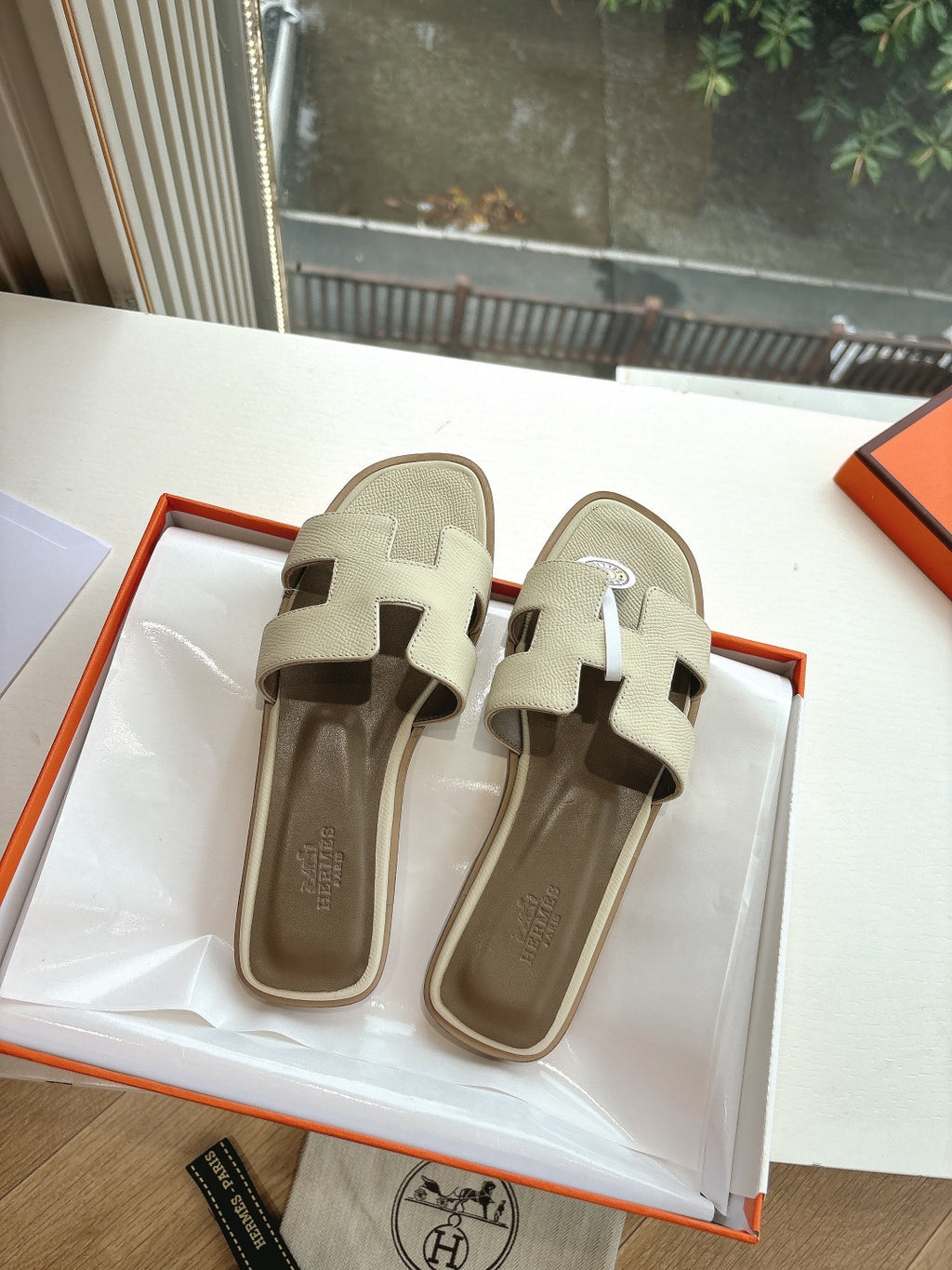 Hermes slide sandals in light beige, front view with logo emblem on strap