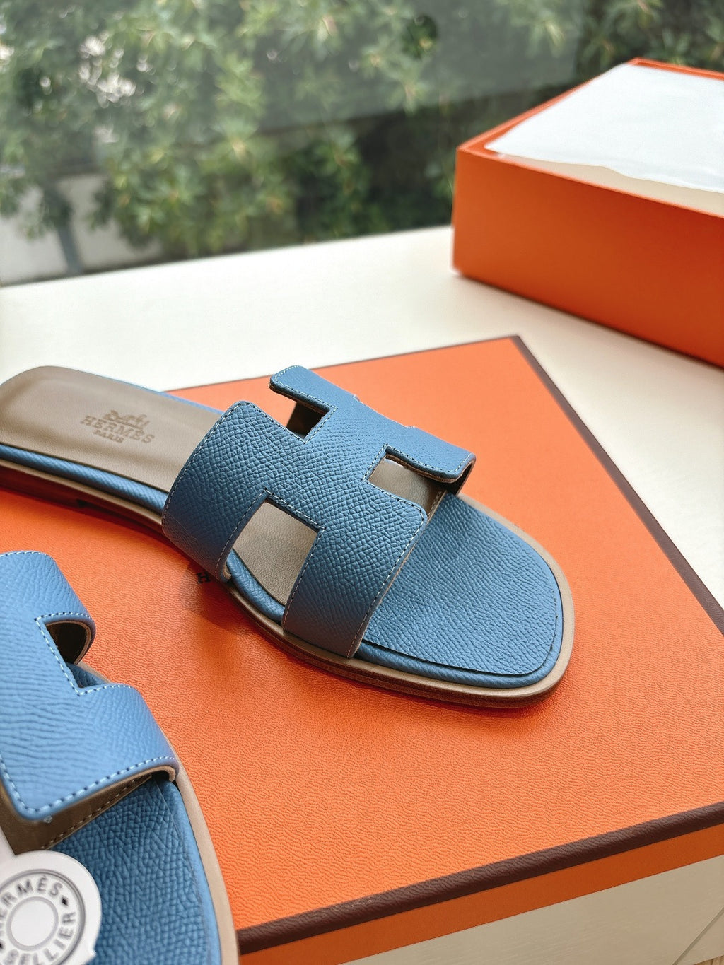 Close-up of blue Hermes slide sandals with embossed H cutout on textured strap