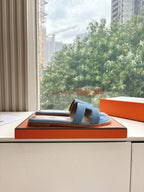 Blue Hermes slide sandal on orange box, showing single-strap H detail