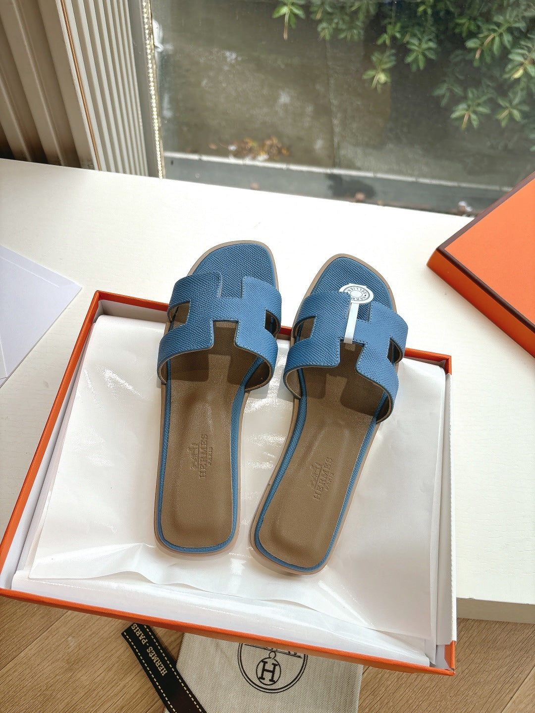 Pair of blue Hermes slide sandals with H cutout, side-by-side on display