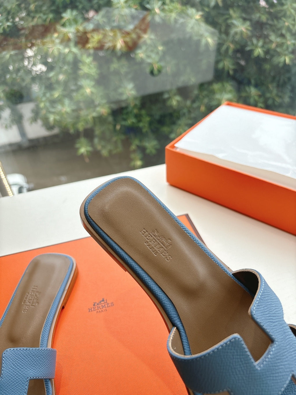 Close-up of blue Hermes slide sandals showing tan insoles and H cutout openings