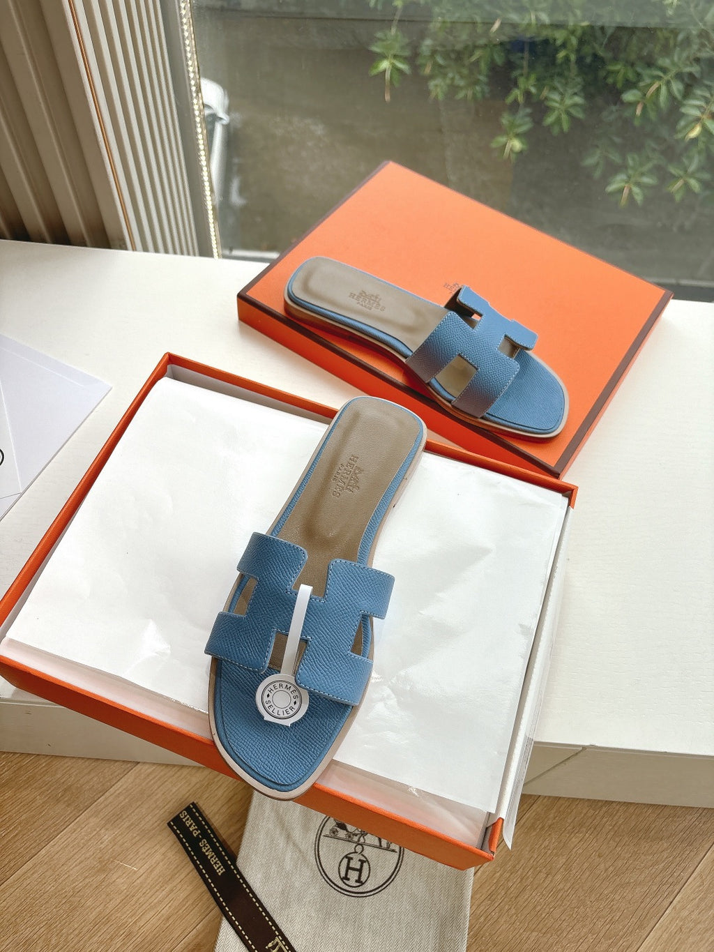 Blue Hermes slide sandals with H cutout, shown top view in orange gift box