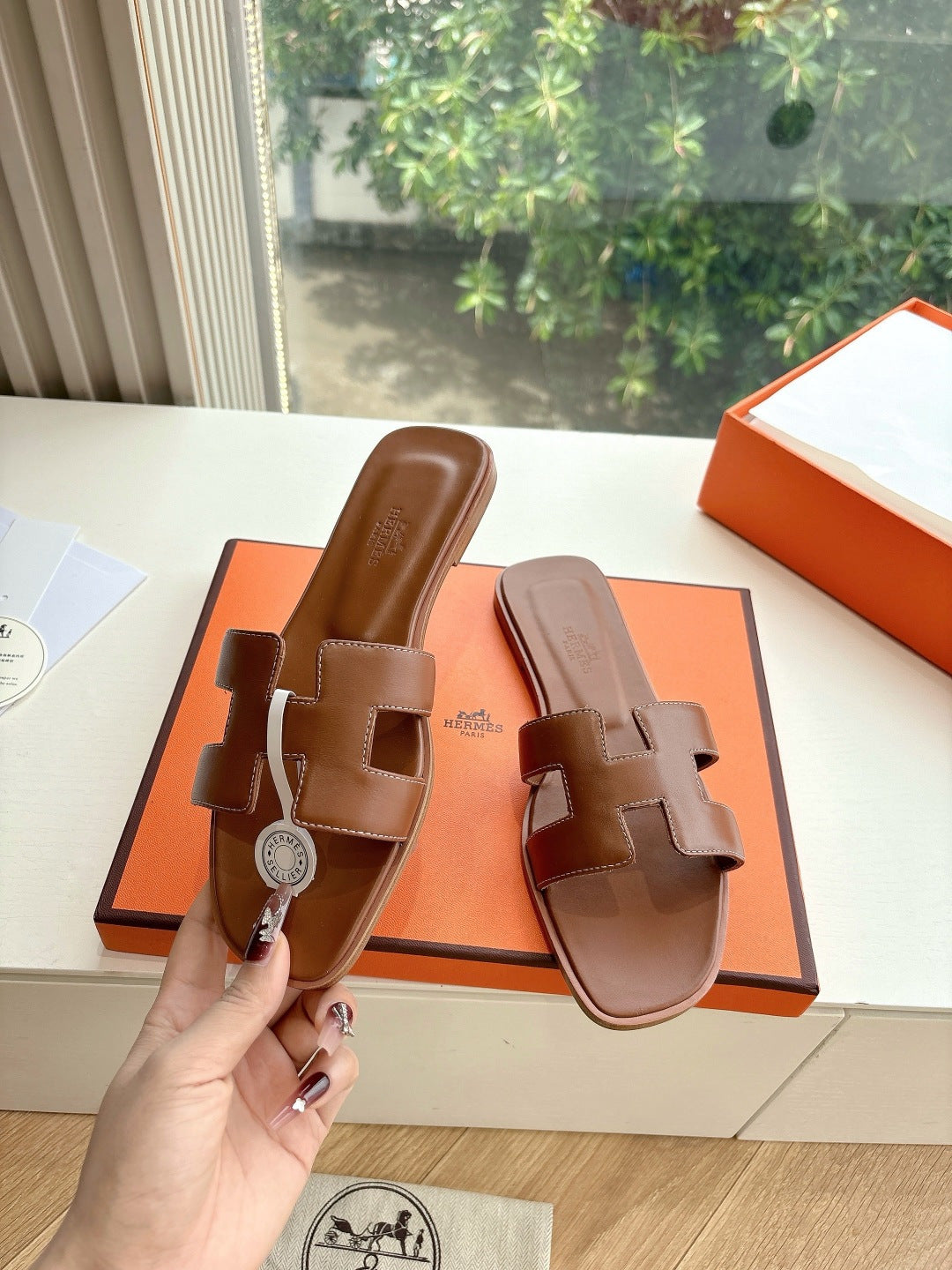 Hermes women's brown leather slide sandals, hand holding, side view