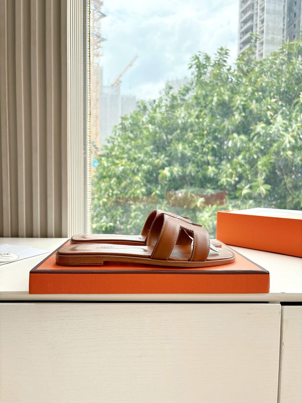 Hermes women's brown leather slide sandals, profile view on orange box