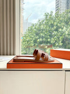 Hermes women's brown leather slide sandals, profile view on orange box