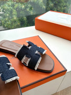 Hermes slide sandal close-up on orange box, brown leather with dark navy cross strap
