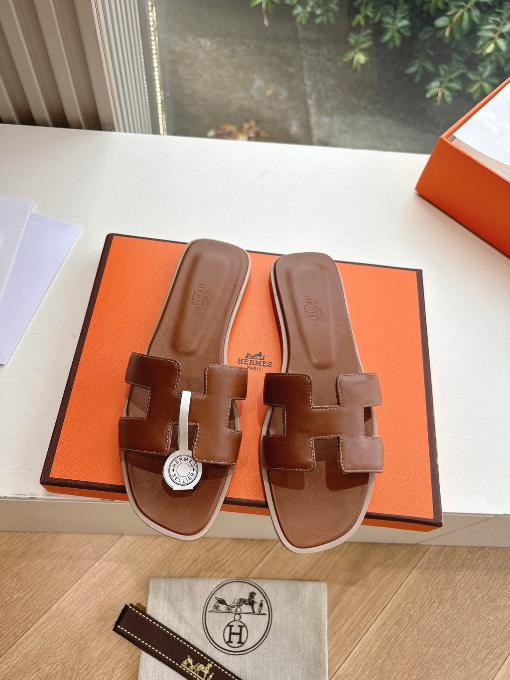 Hermes leather slide sandals pair on orange box, brown with logo hardware