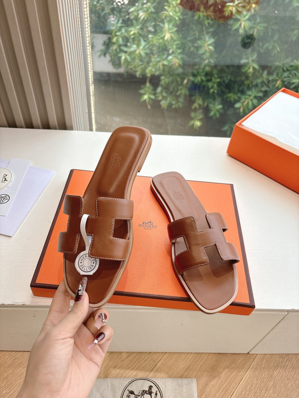 Hermes leather slide sandals held in hand, brown with logo medallion strap