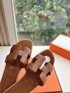 Hermes leather slide sandals close-up of straps and logo medallion, brown