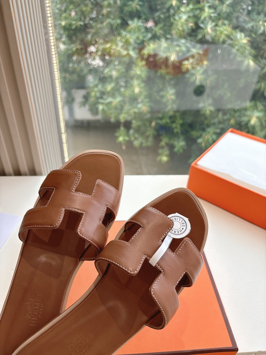 Hermes leather slide sandals close-up of straps and logo medallion, brown
