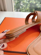 Hermes women's tan slide sandal close-up, logo charm on side strap and leather sole