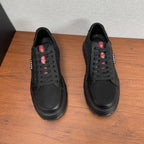 Black lace-up sneakers, front view with chunky rubber sole and red PRADA logo accents