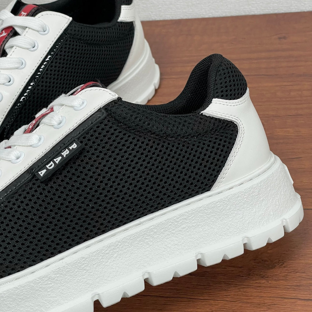 Prada unisex sneakers side close-up, black mesh upper with white trim and logo stripe