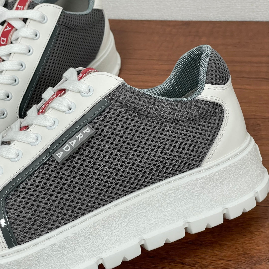 Prada unisex sneakers close-up side: gray perforated mesh, white leather trim, logo patch