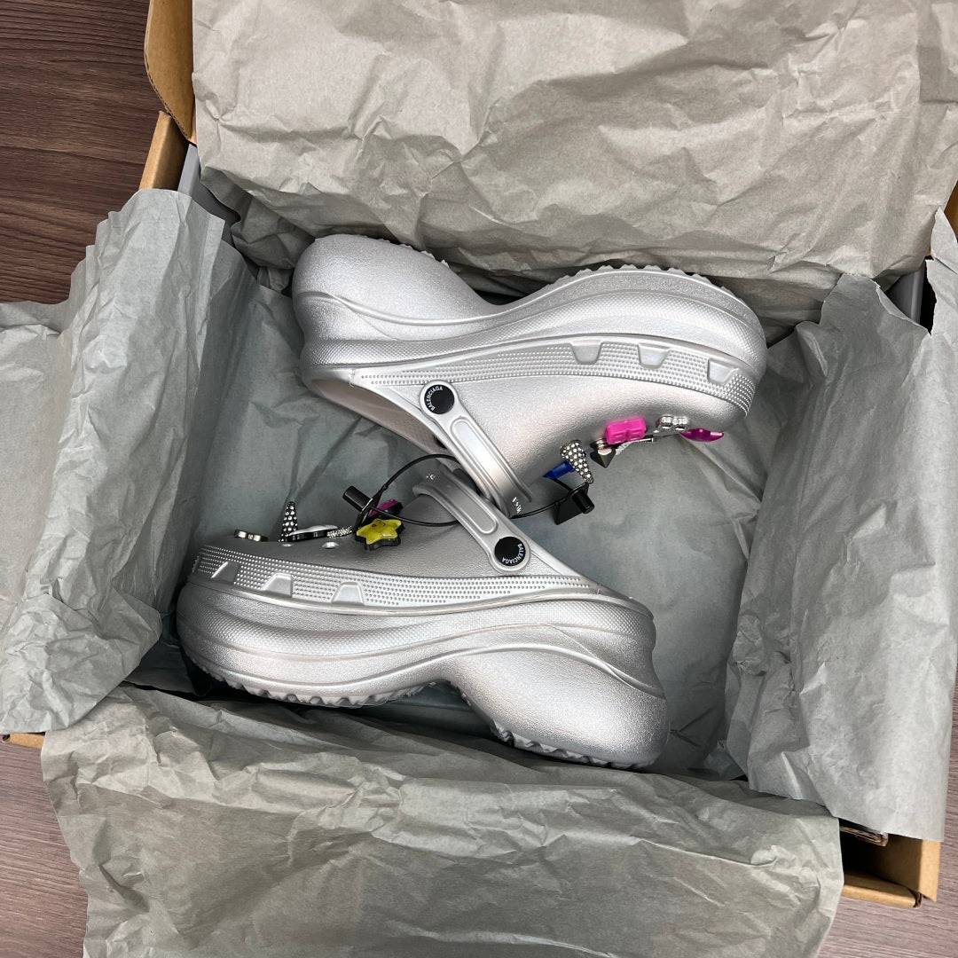 Balenciaga silver platform clogs inside paper packaging, decorated with charms