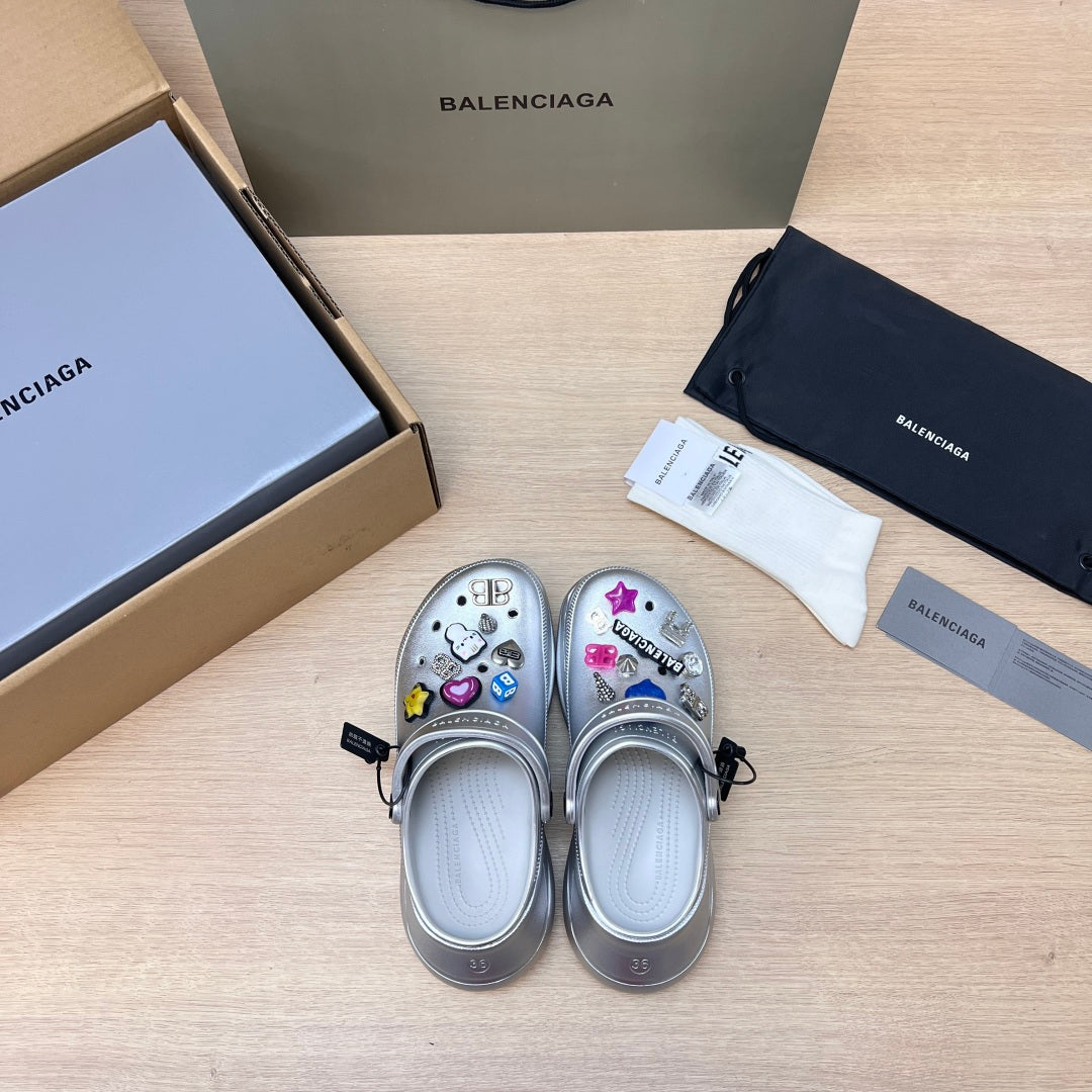 Pair of silver slide clogs with open toe, ventilation holes, and cartoon-style patches