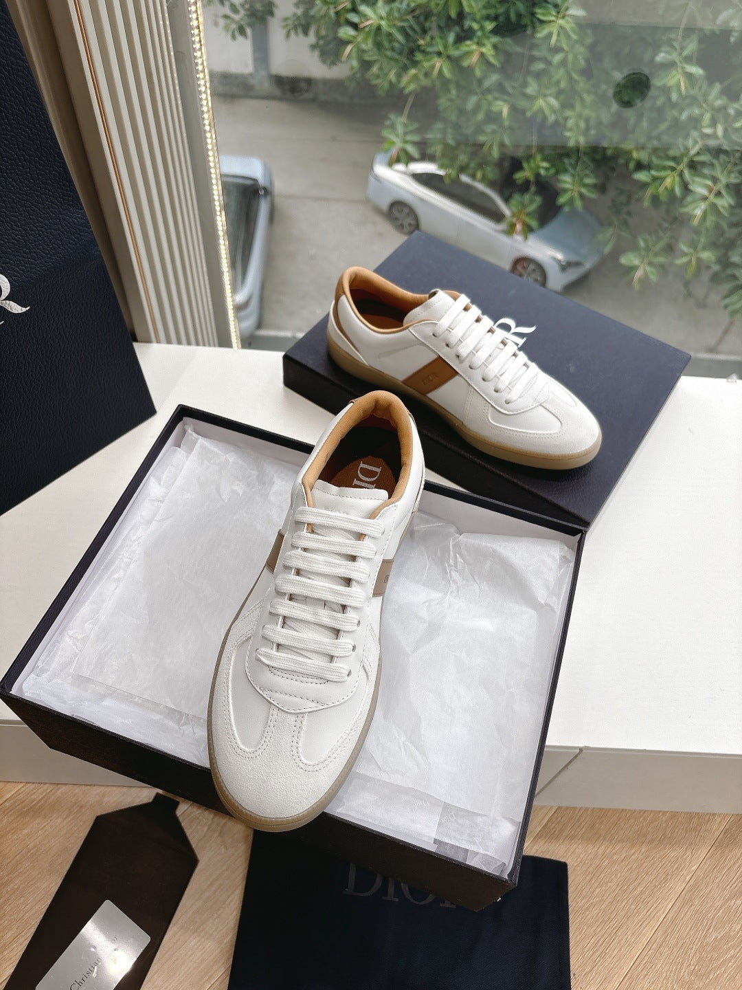 White and tan lace-up unisex sneakers on black boxes, front view