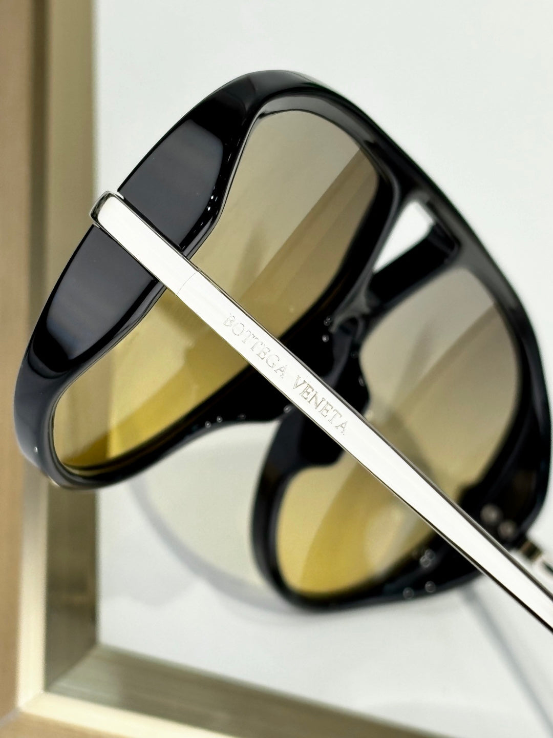 Black sunglasses with gold-tone bar and “Bottega Veneta” branding detail