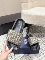 Dior slide sandals held in hand, beige logo pattern straps over black footbeds