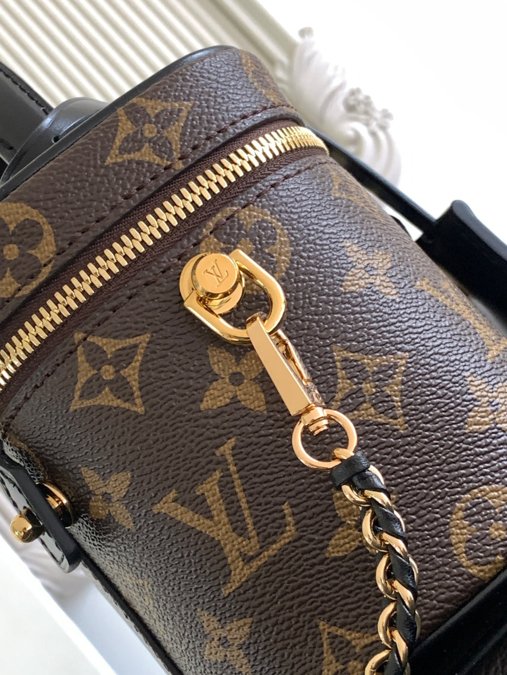 Louis Vuitton monogram bag close-up with gold zipper pull and attached chain strap.