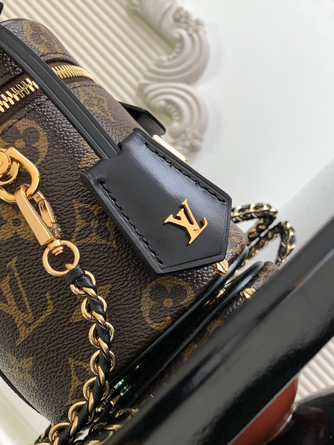 Louis Vuitton monogram bag detail with black leather patch, gold hardware, and chain strap.