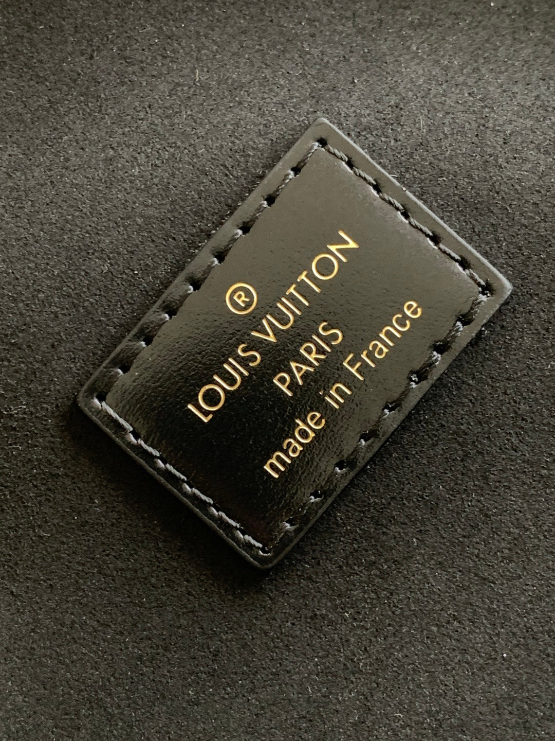 Louis Vuitton label with "PARIS" and "made in France" stitched on dark fabric.