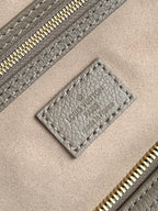 Louis Vuitton bag close-up: taupe leather label and gold zipper on textured grain